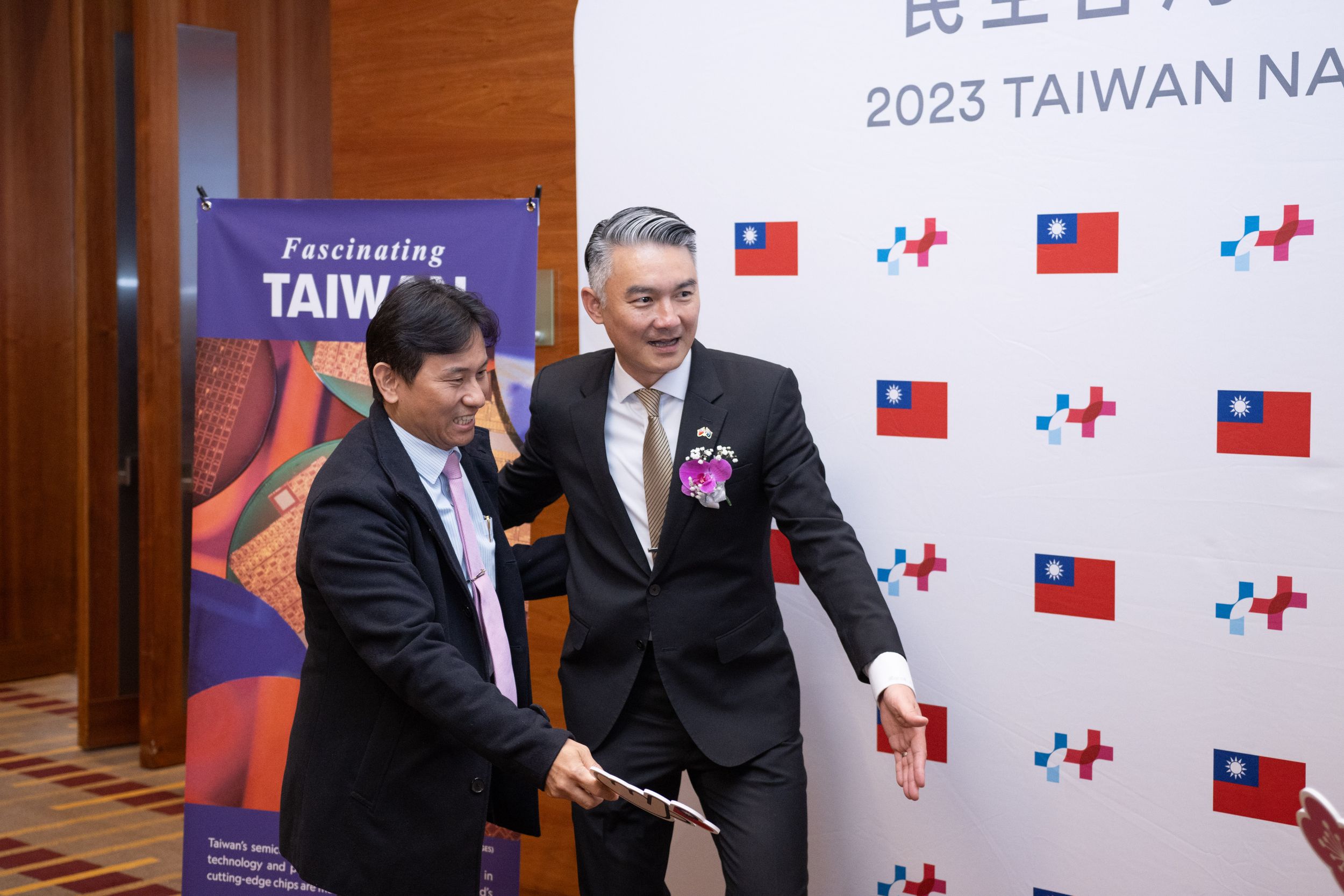 Professional handshake between two people at Taiwan-themed event with flags displayed.