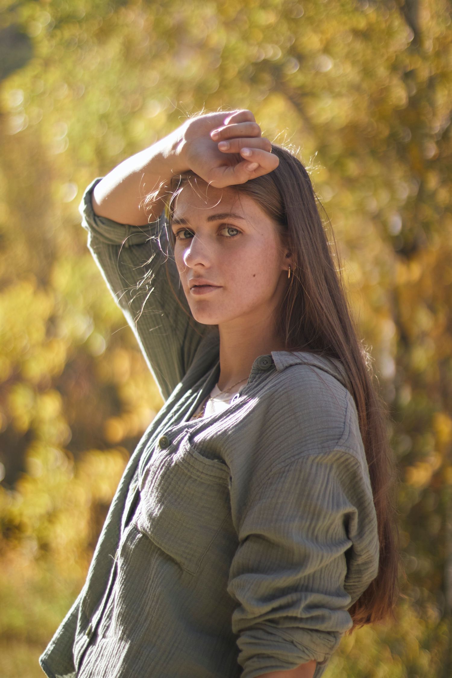 Woman posing outdoors in soft golden sunlight, wearing a green shirt, surrounded by autumn foliage for a warm, natural portrait vibe.