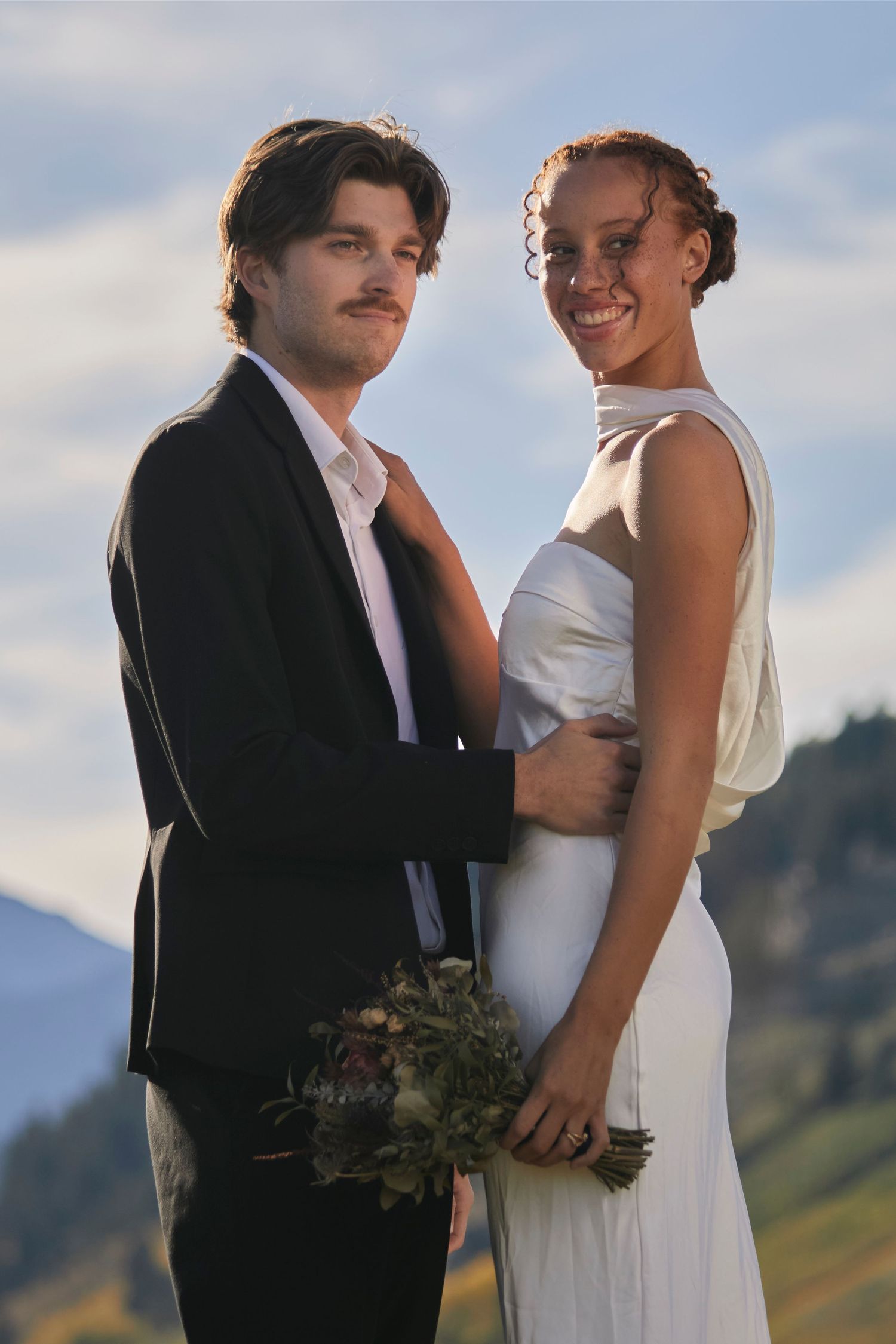 Wedding couple photography outdoor with soft light. Woman holding flower bouquet and man holding his bride's waist