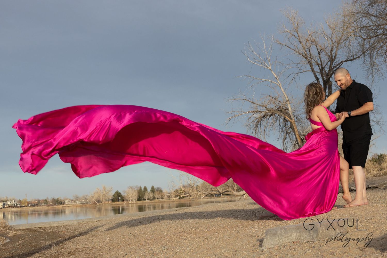 Dramatic shot of flowing pink dress caught in wind against lakeside landscape.