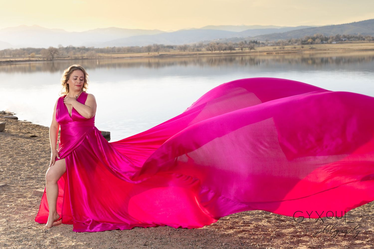 Bright pink flowing dress creates dramatic movement against serene lake backdrop.