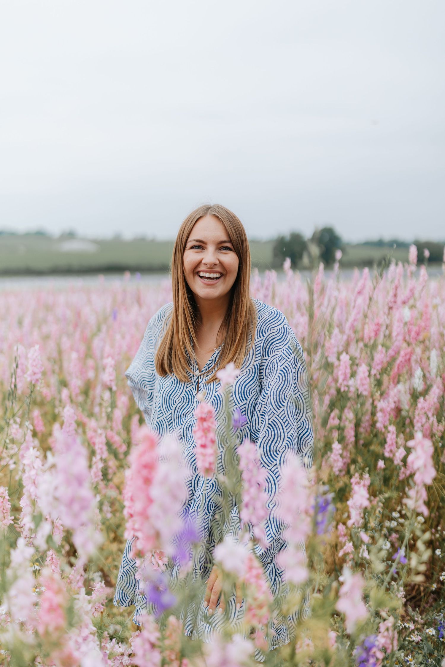 Rebecca May stands joyfully in a field of pink and purple wildflowers on a misty morning. Rebecca May Photography - Shropshire