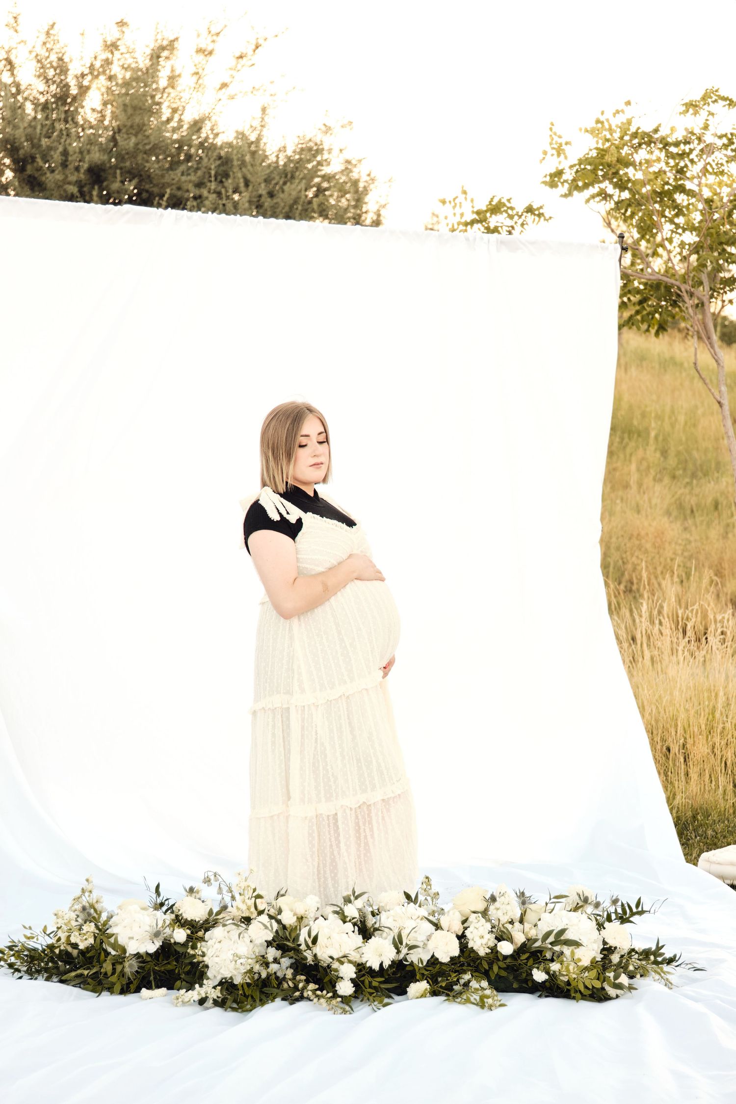 Expecting mother caressing her belly in an outdoor styled photoshoot with fresh flowers