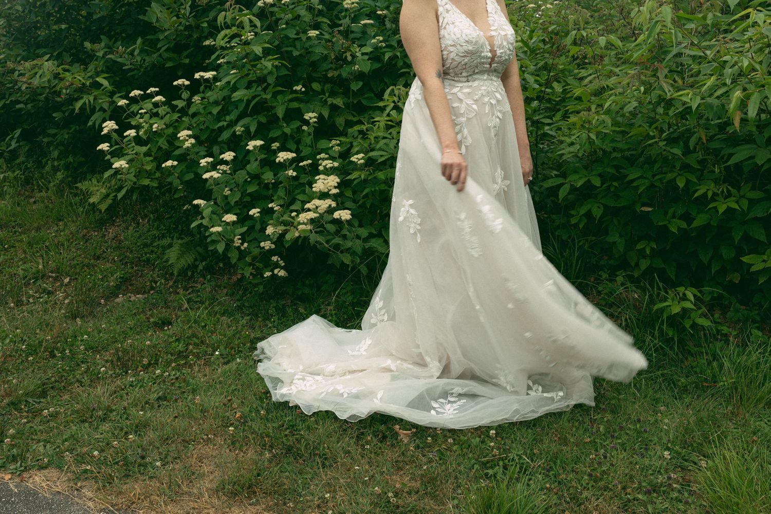 A flowing white lace wedding dress with delicate details trails along a garden path.