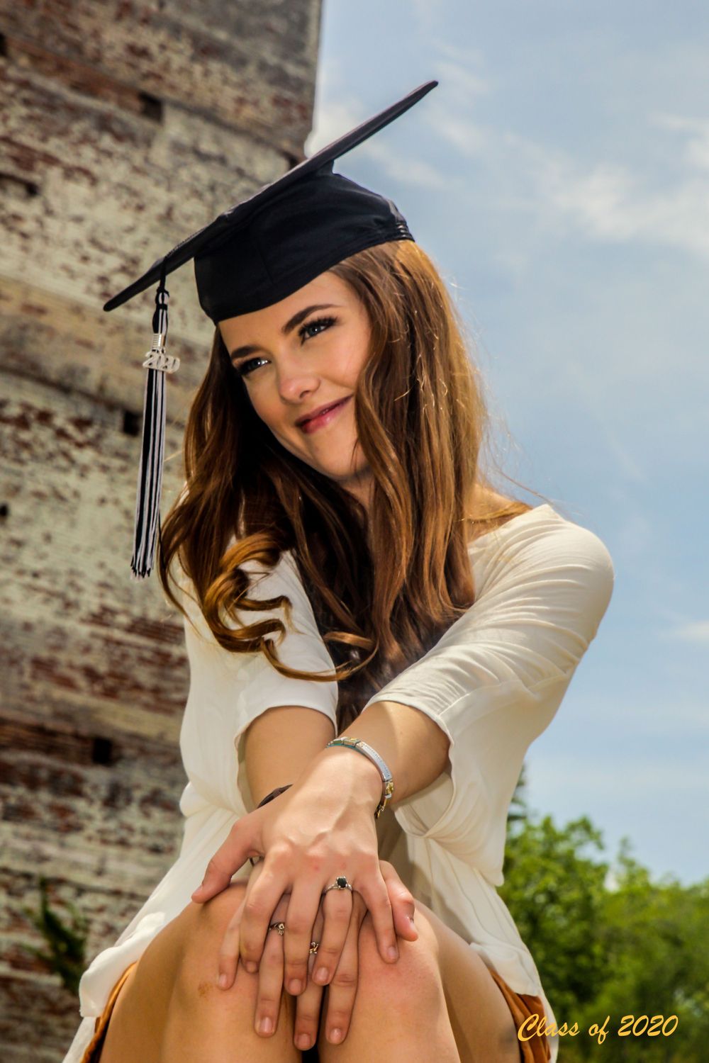 A Class of 2020 graduate smiles while posing outdoors wearing a black graduation cap.