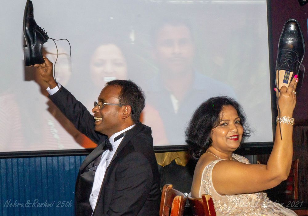 Couple laughing and holding up shoes during fun wedding reception game at formal event.