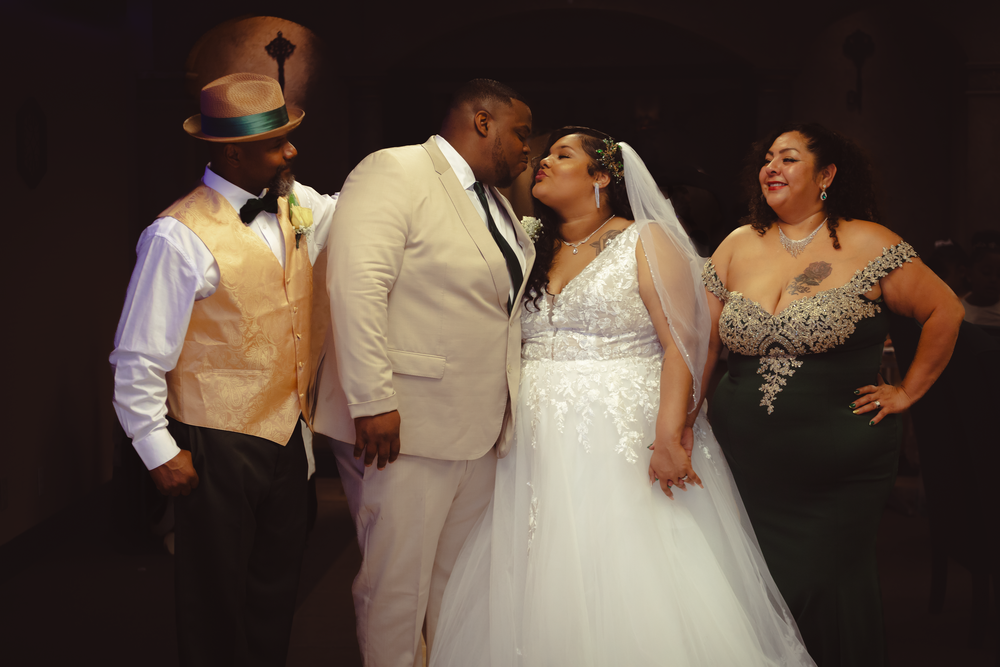 Bride and groom sharing kiss with wedding party members nearby.