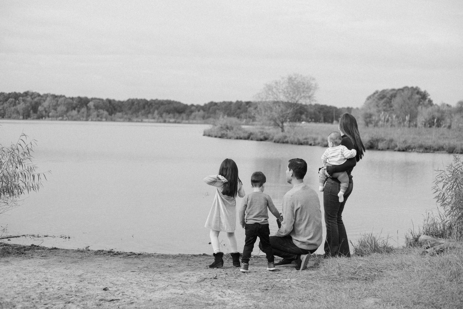 Black and white silhouette of family standing together by lakeside.