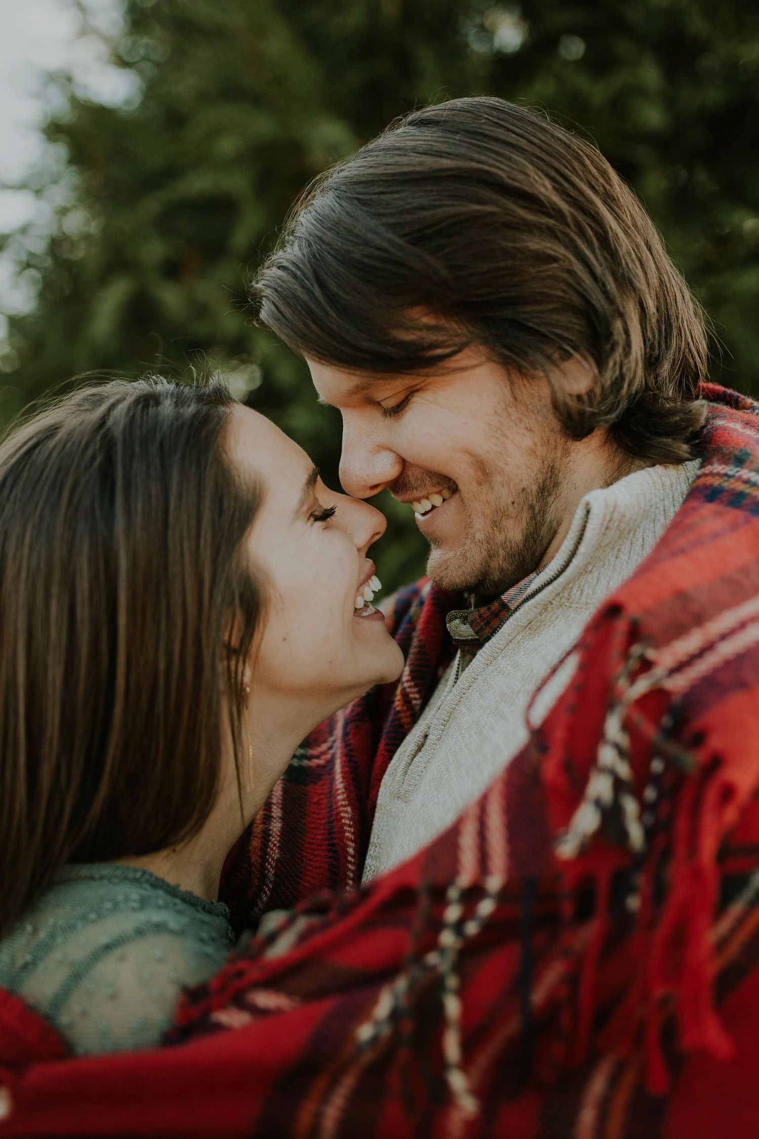 Intimate moment between couple wrapped in red blanket during outdoor photo session.