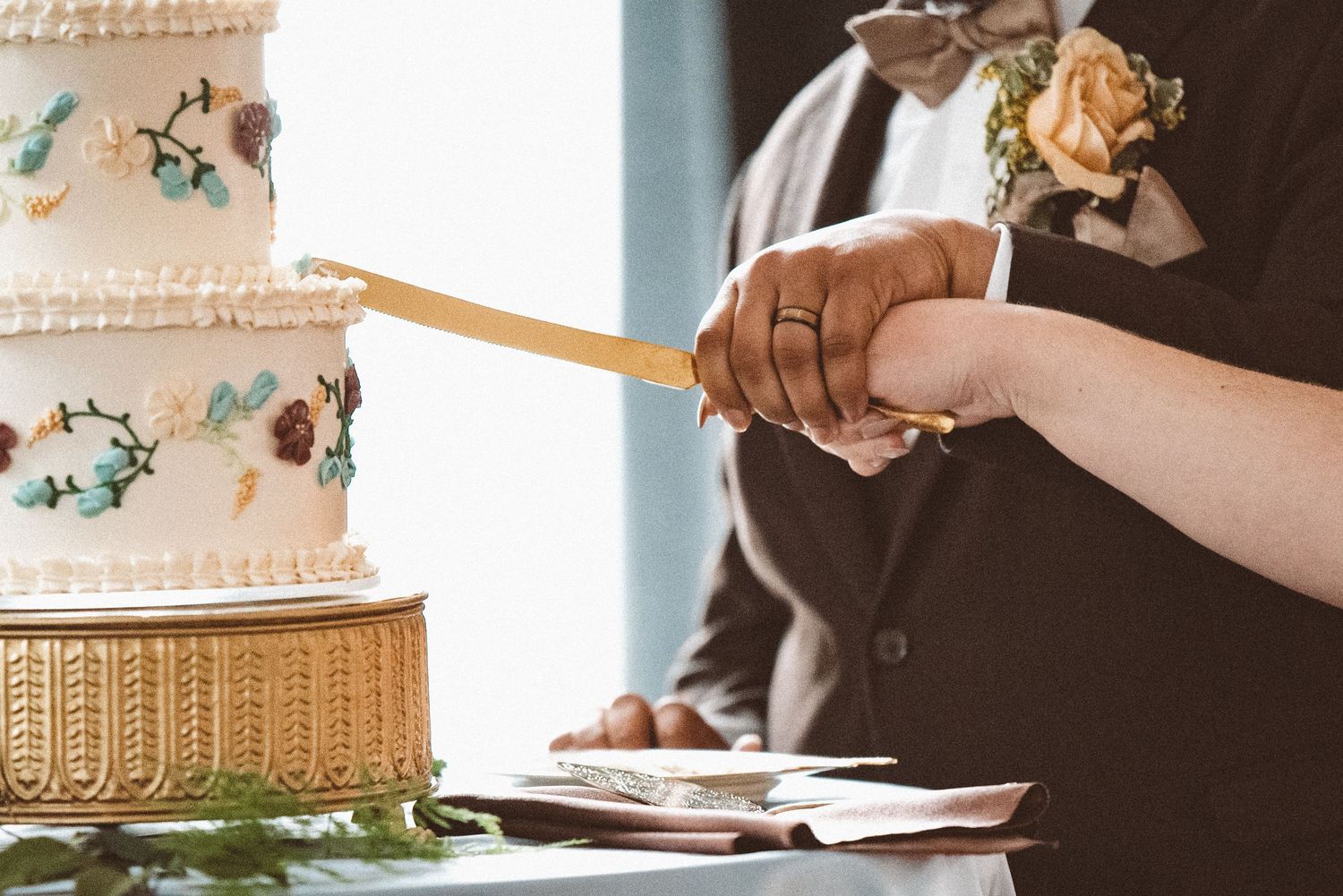 A zoomed-in image of a couple cutting their wedding cake with a gold cake knife.