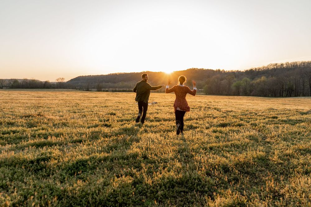 ©AnnaVonRiesenPhotography Engagement Portrait | Color image of a couple running across a field into the sunset together