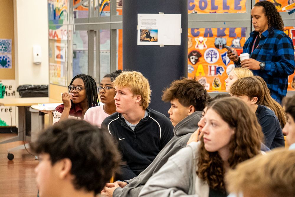 Students sit attentively during class instruction in a bright classroom decorated with colorful artwork on the walls.
