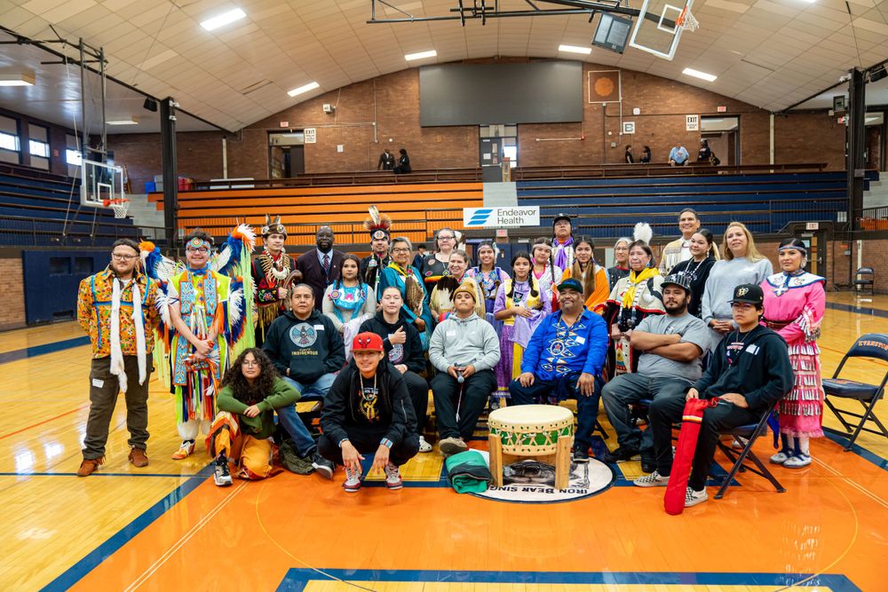 Large group of students and staff gather together on gym floor for group photo in school gymnasium.