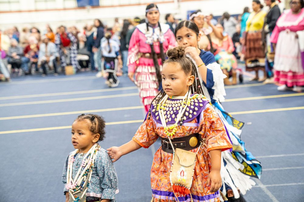 Traditional dancers in colorful regalia walk together during a Native American powwow celebration.