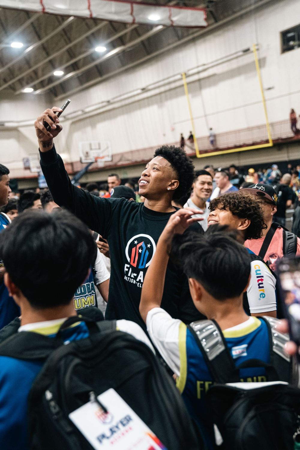 Excited youth takes selfie during crowded event at indoor sports venue.