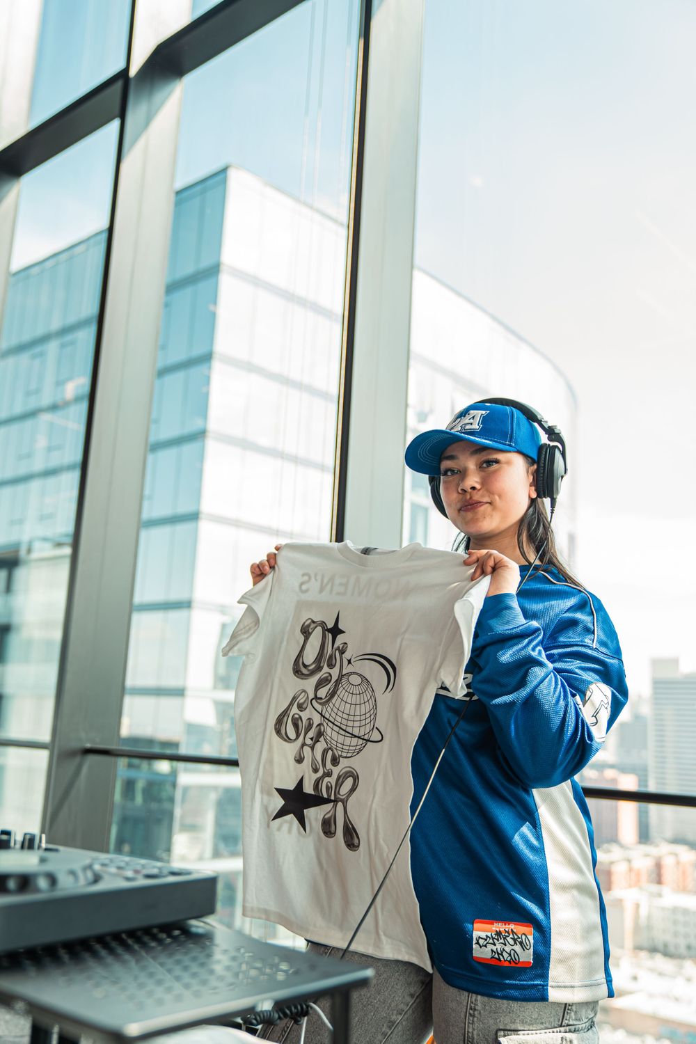 Artist in blue jacket and cap displays custom artwork design against modern glass building.