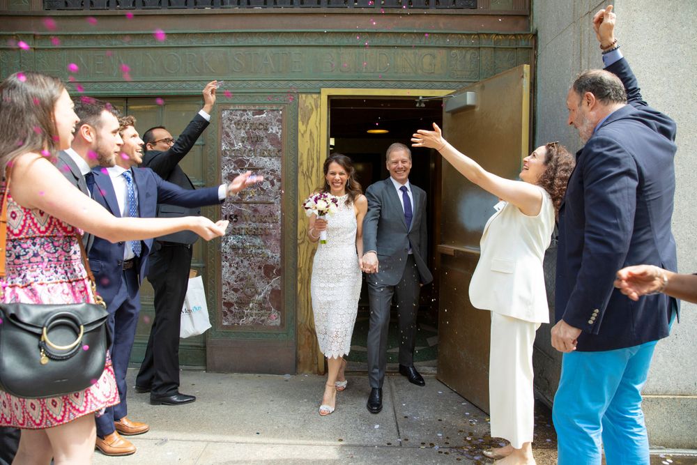 Wedding guests with raised arms celebrate as newlyweds exit a NYC Clerks office.
