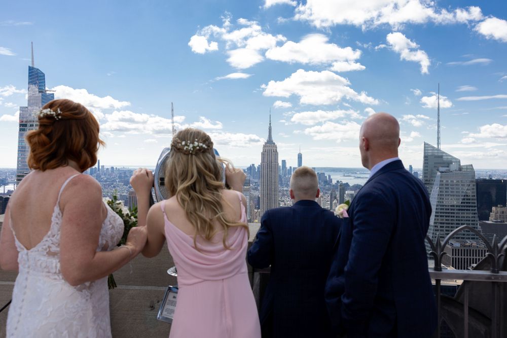 Wedding group admiring New York City skyline from observation deck at Top of the Rock.