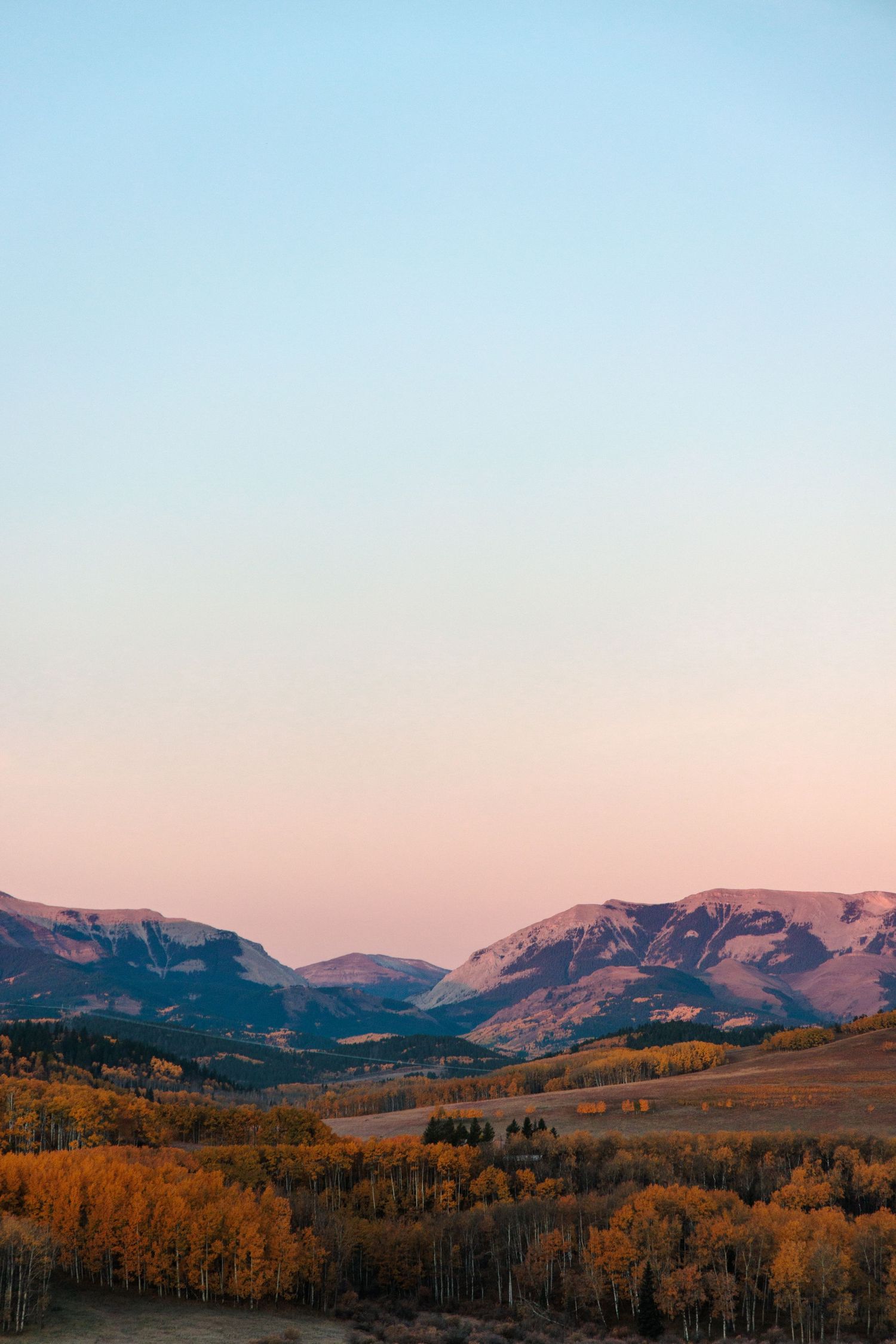 Scenic mountain valley with golden autumn trees against pink and blue sunset sky.