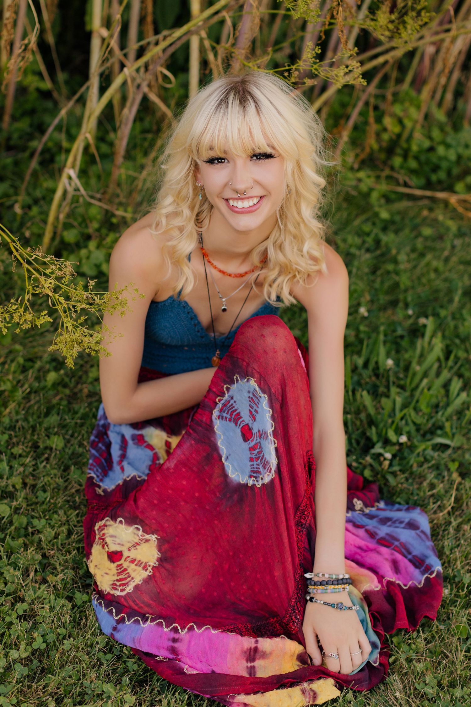 Woman wearing blue top and red tie-dye skirt sitting on grass in outdoor setting.