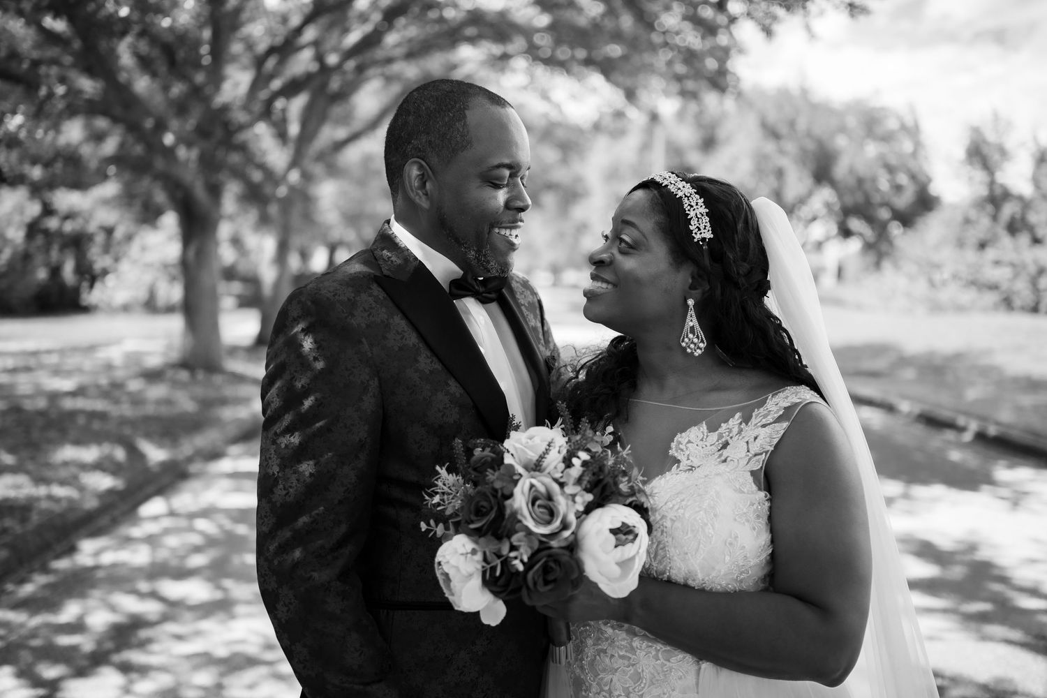 Black and white outdoor wedding portrait capturing joyful interaction between bride and groom.