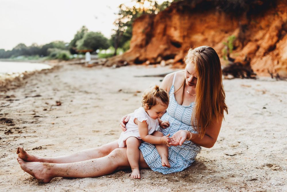 A tender beach moment shared between parent and child on sandy shore with orange cliffs.