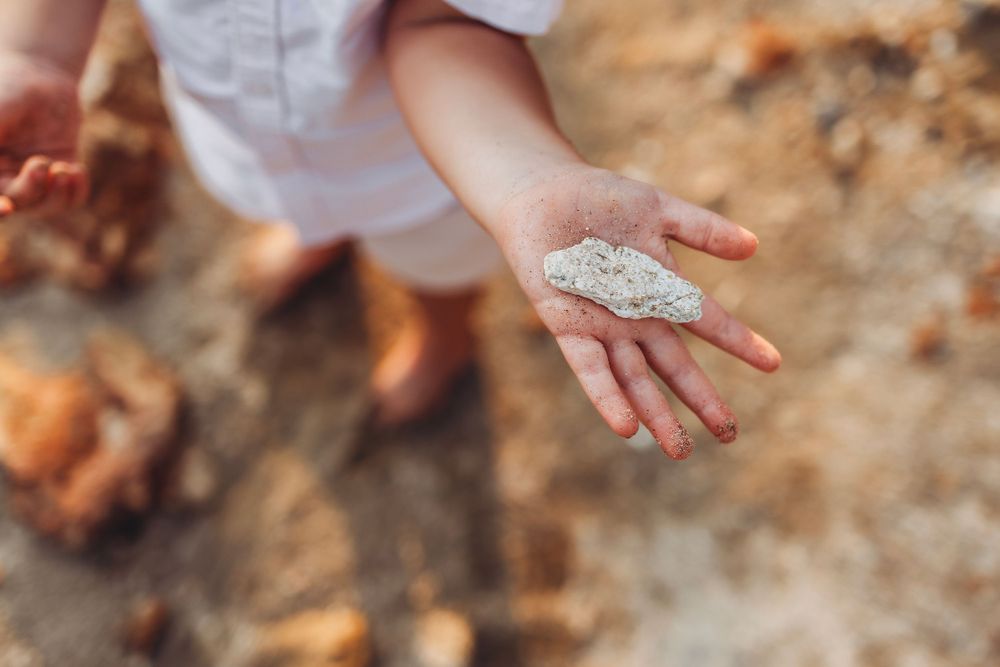 A close-up shot of a small hand holding sand on the beach.