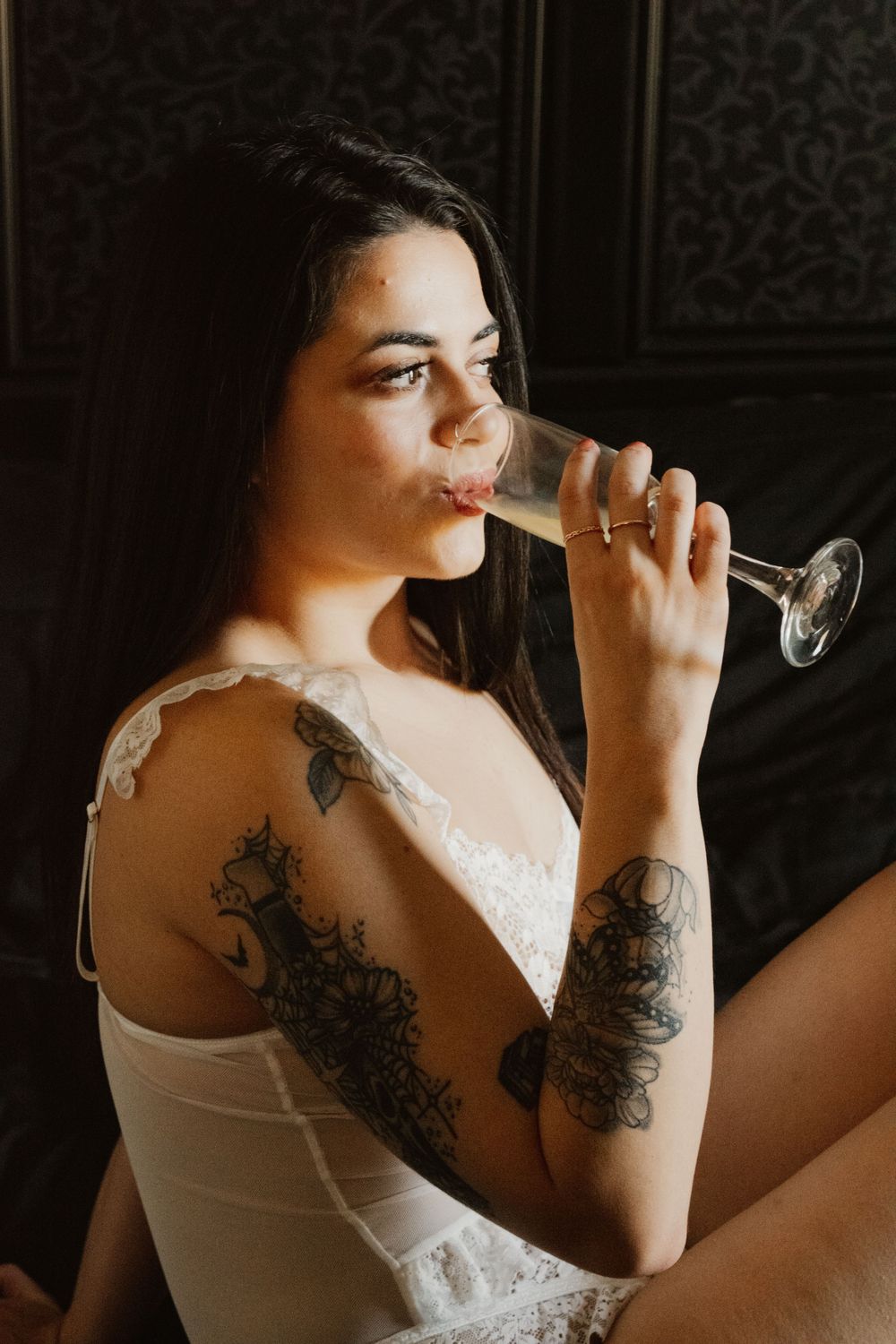 A series of artistic boudoir photos showing a woman in white lace drinking from a wine glass against a dark background.