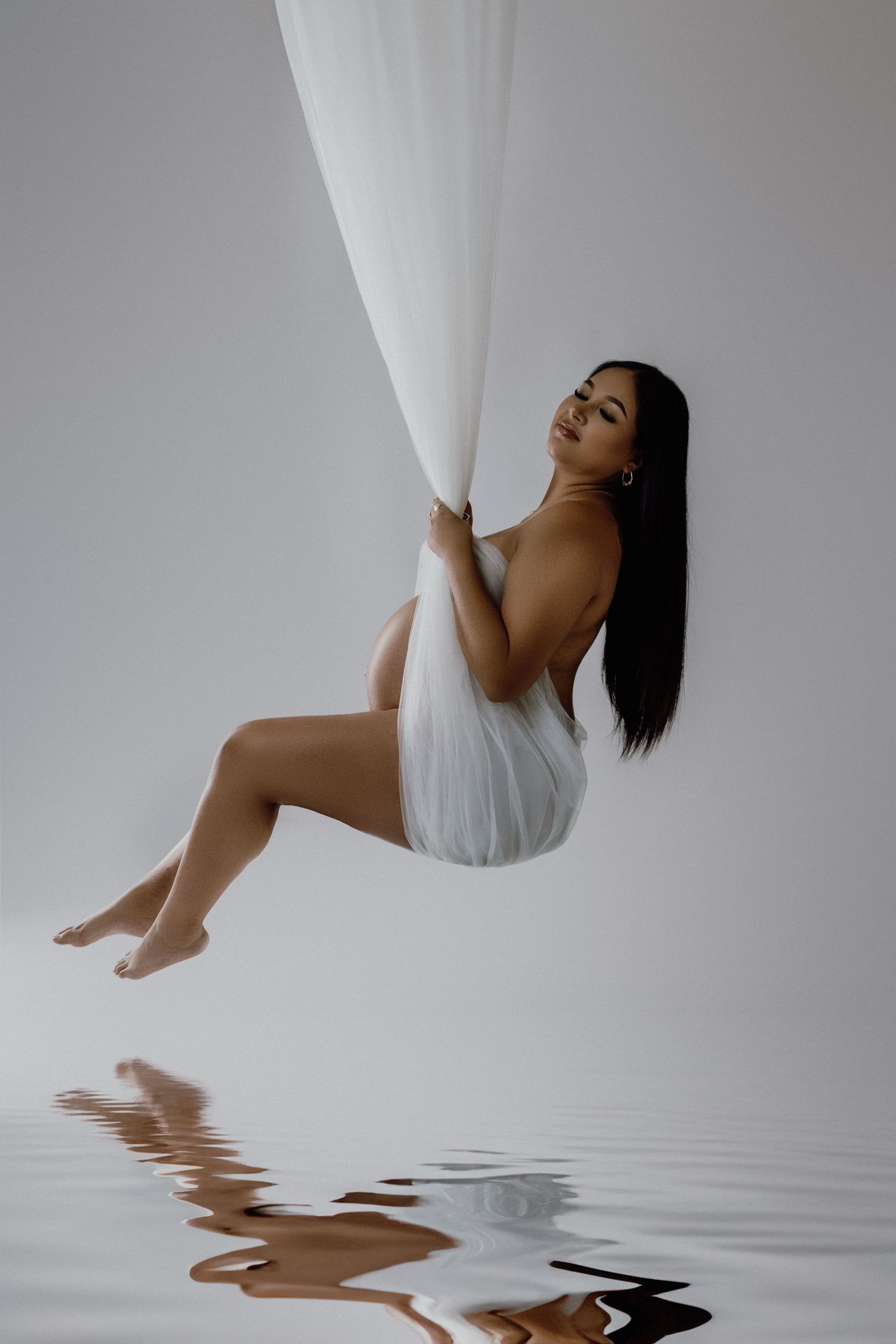 Ethereal portrait with flowing white fabric against minimalist background with water reflection.