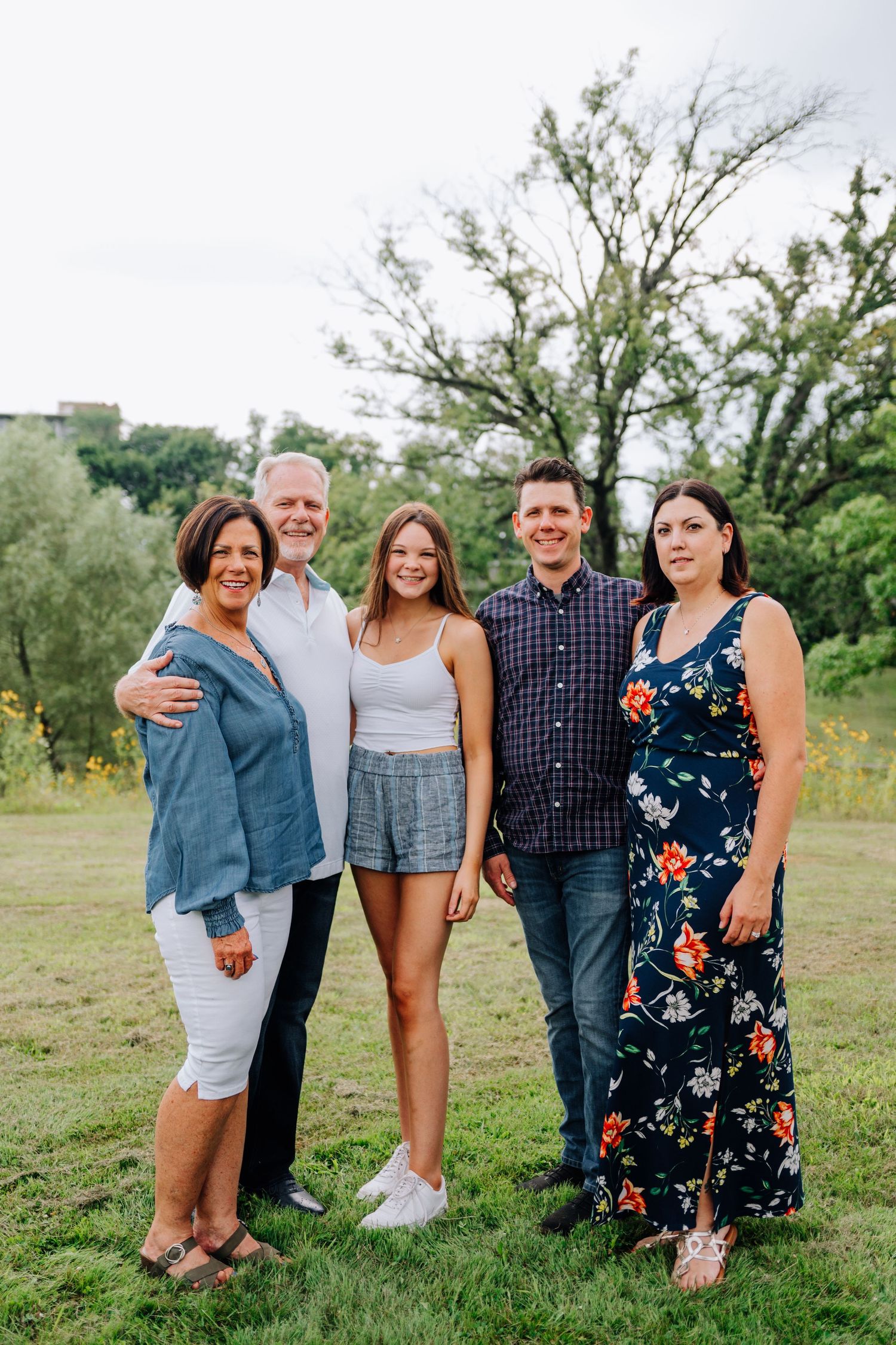 Group portrait of five people outdoors with trees and natural scenery in background.
