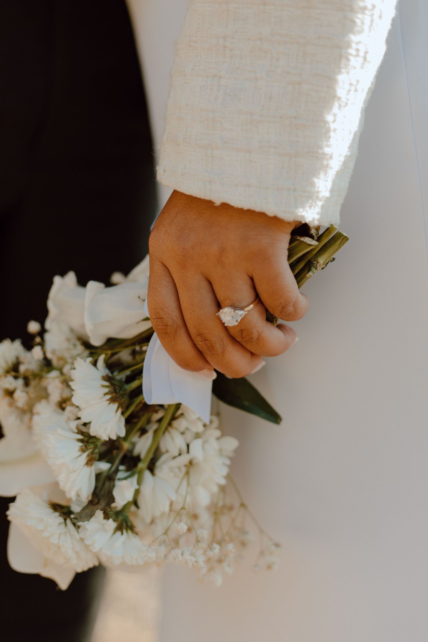 Close-up of bride's hand holding white floral bouquet with engagement ring prominently displayed.
