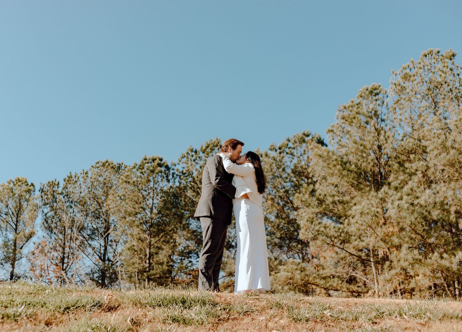 A couple shares a romantic moment on a hilltop against a backdrop of autumn trees and blue sky.