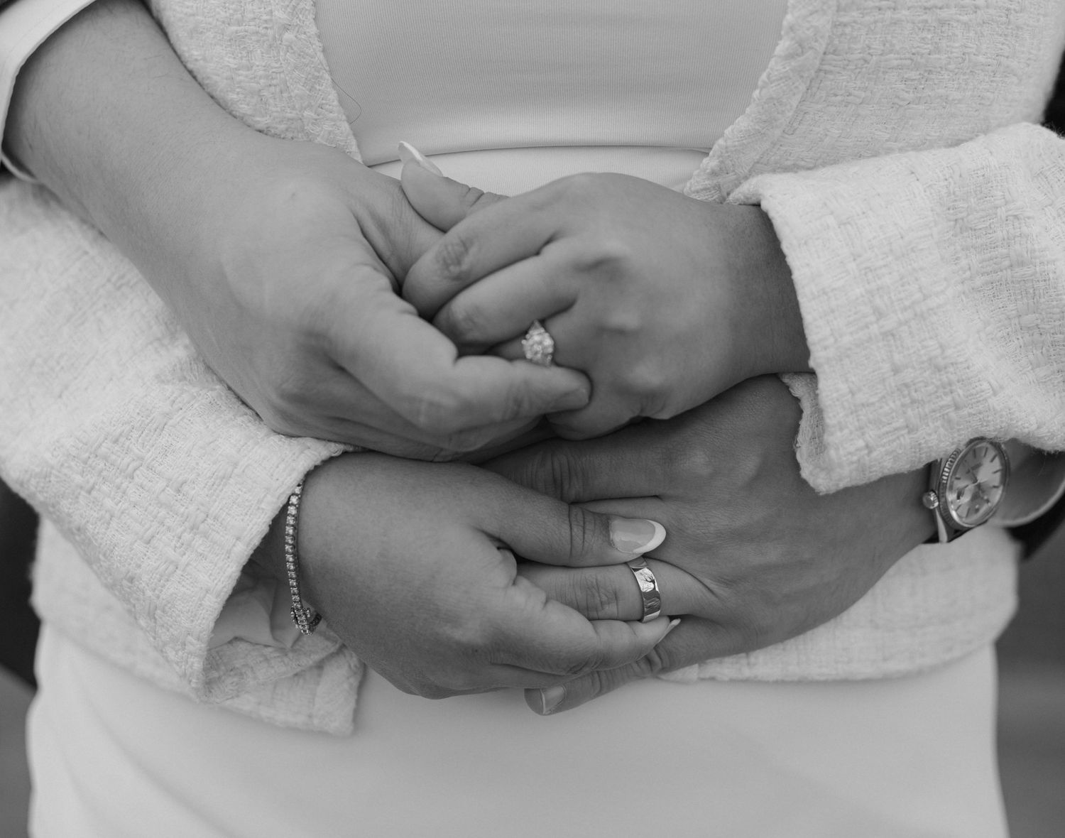 Black and white close-up of hands wearing wedding rings gently clasped together.