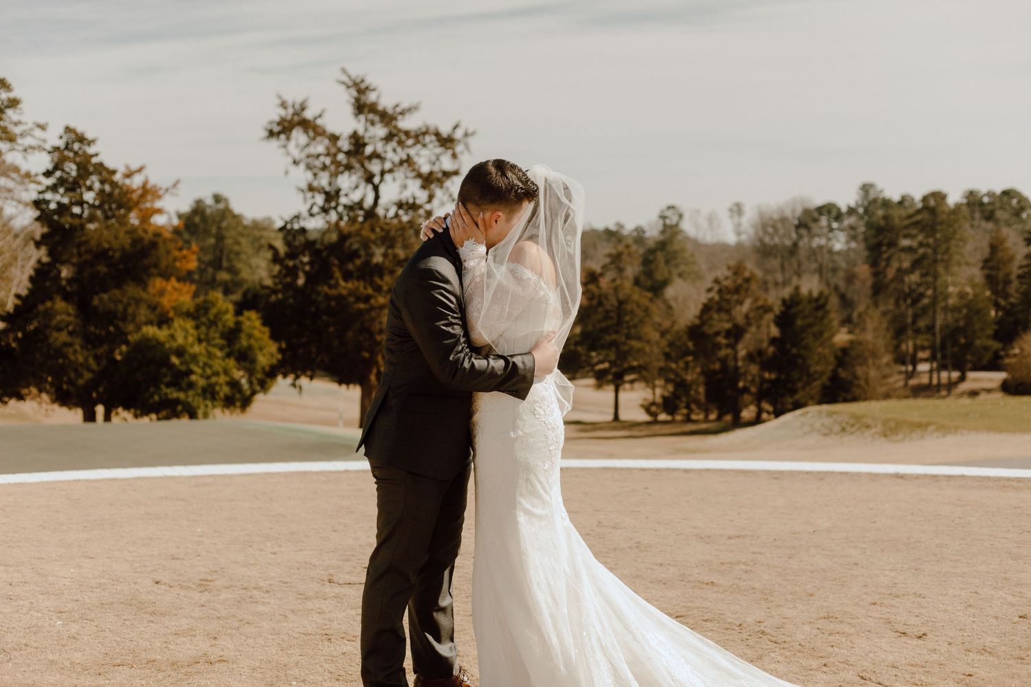 A couple in wedding attire embraces on a scenic golf course during an autumn day.
