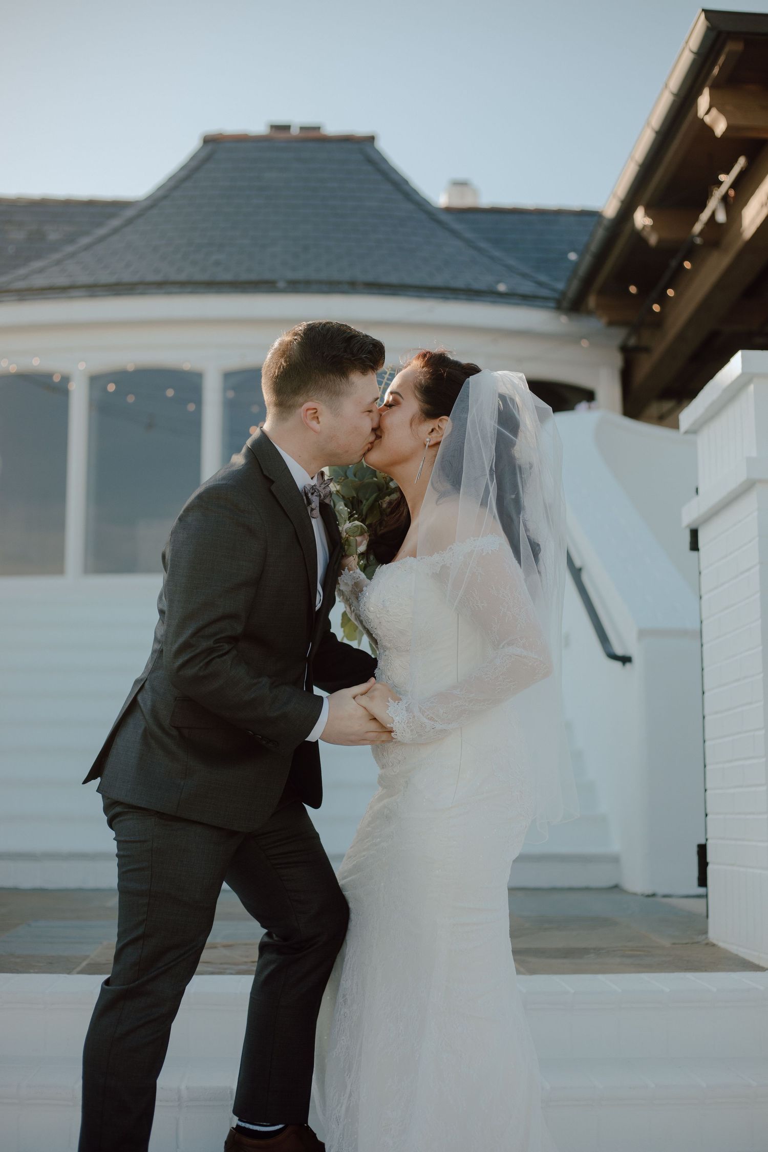 A romantic wedding moment captured outdoors with a beautiful white dress and dark suit against an elegant building backdrop.