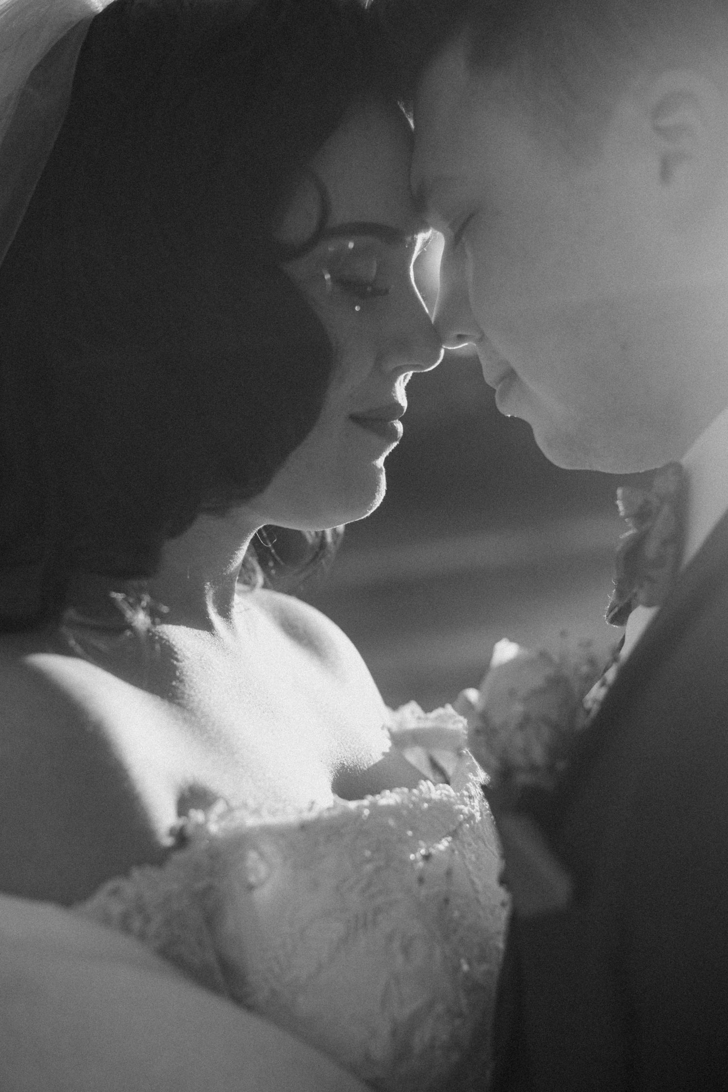 A romantic black and white wedding photo showing a tender moment between newlyweds in an intimate close-up.