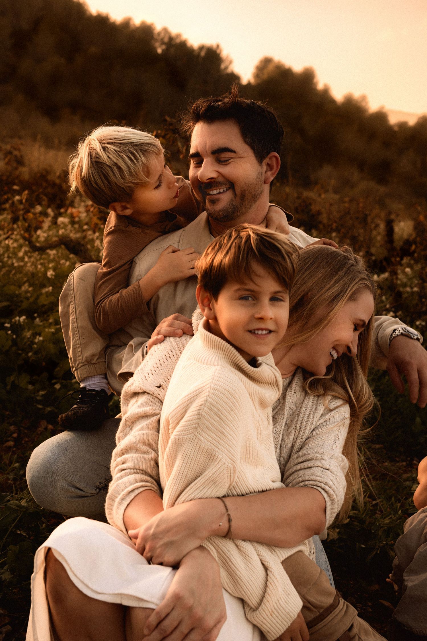 A family in Denia wearing cozy sweaters embraces outdoors during golden hour sunset in an autumn field. Denia family photographer