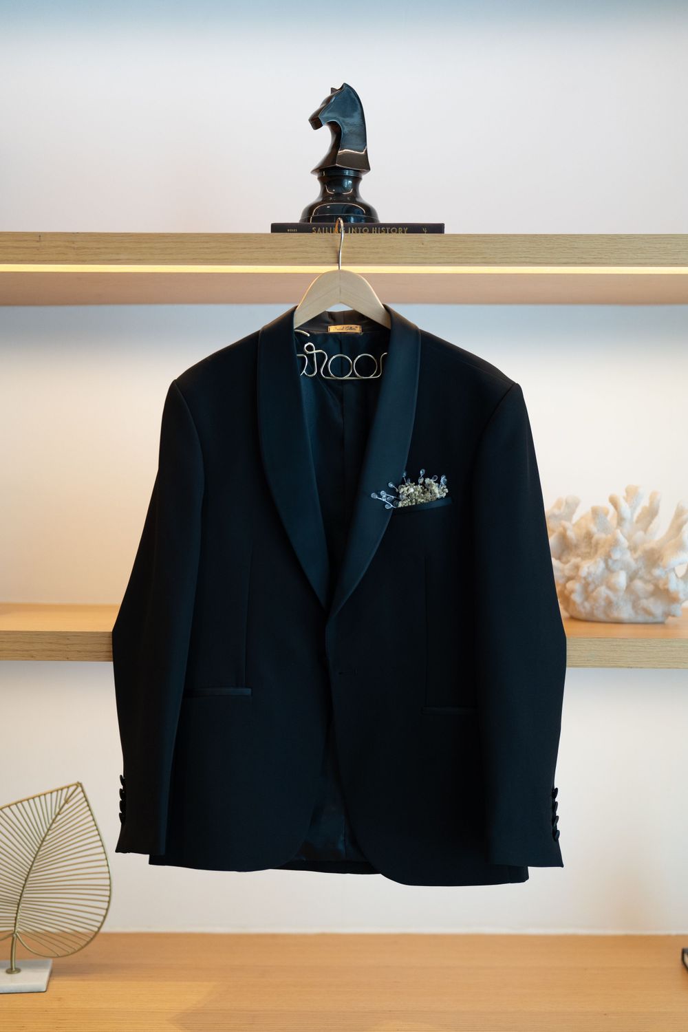 Navy blue groom's suit jacket hanging on wooden hanger with decorative chess piece.