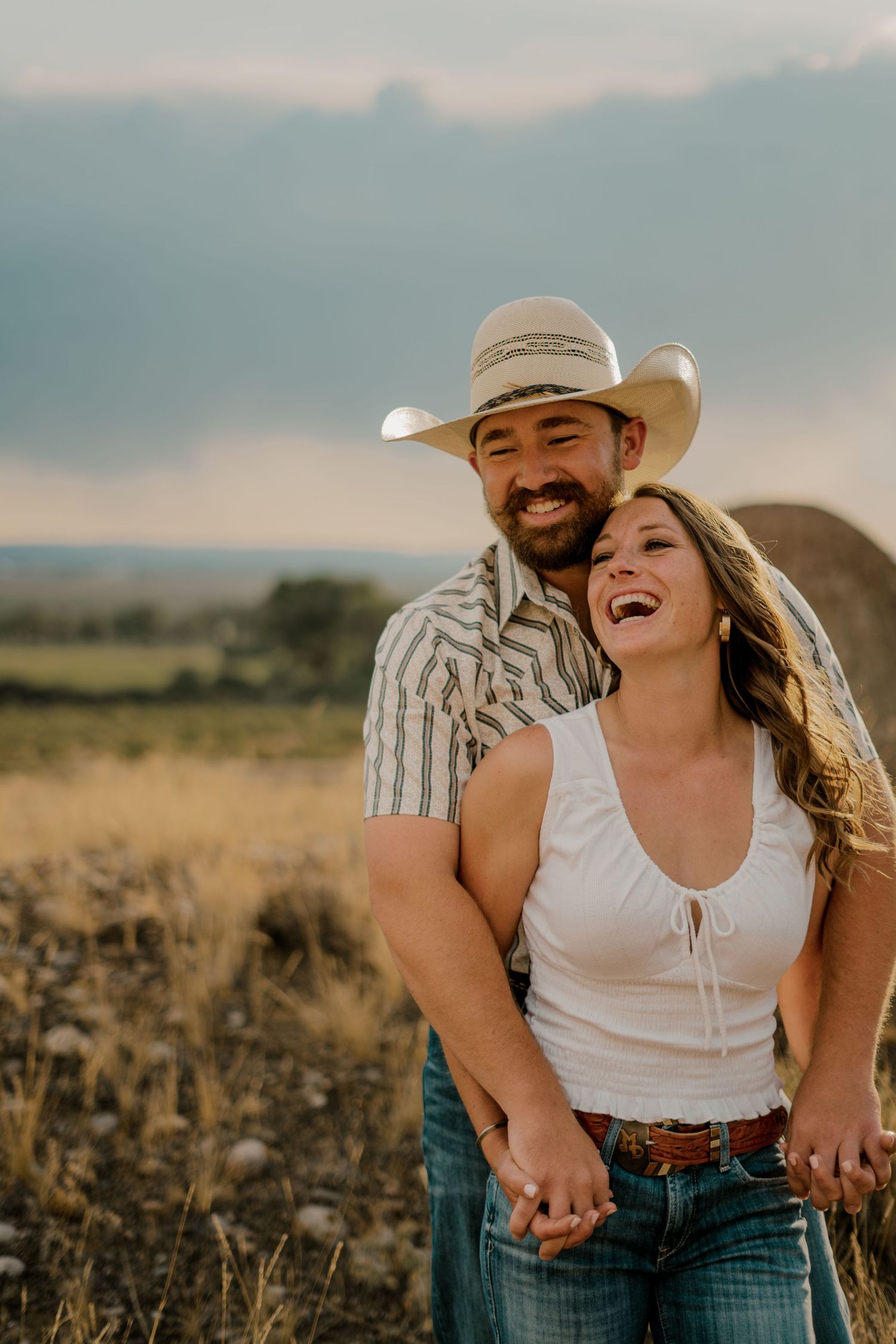 A couple with the man wearing a cowboy hat laughing with a river in the background