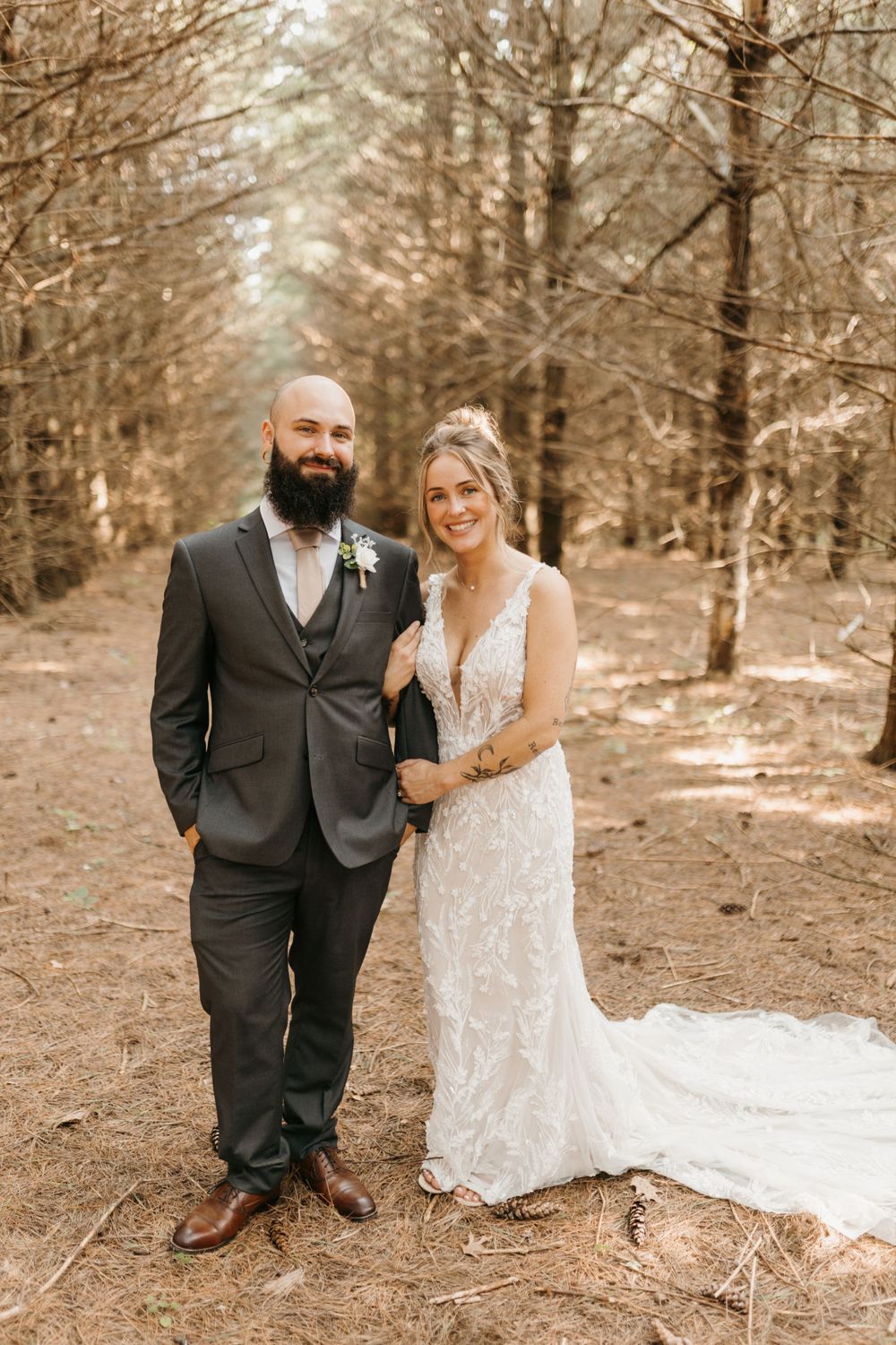 Bride and groom pose together smiling in a tall tree-lined forest path on their wedding day.