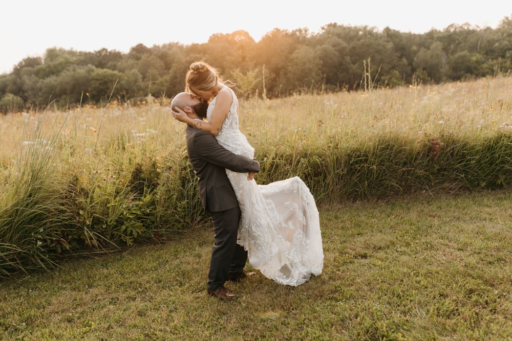 Bride and groom sharing a romantic dip kiss in a sunlit field.