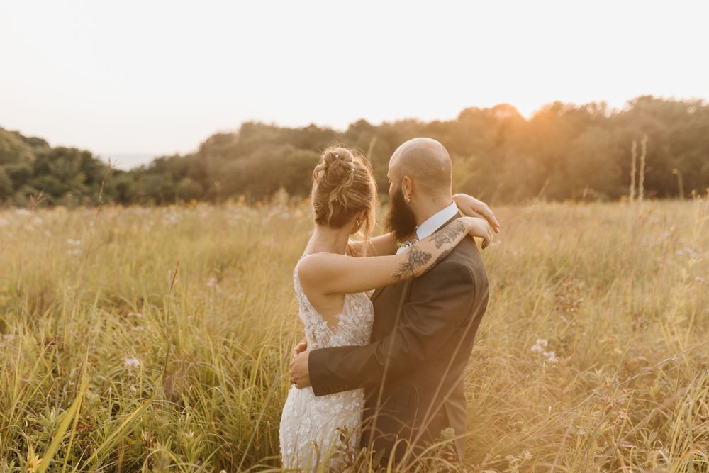 Bride and groom holding each other watching the sunset in a meadow.