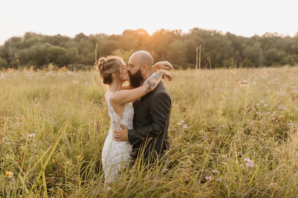 Bride and groom embracing closely in a golden meadow at sunset.