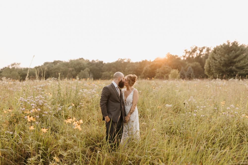 Bride and groom sharing a kiss in a sunlit wildflower field during golden hour at their wedding.