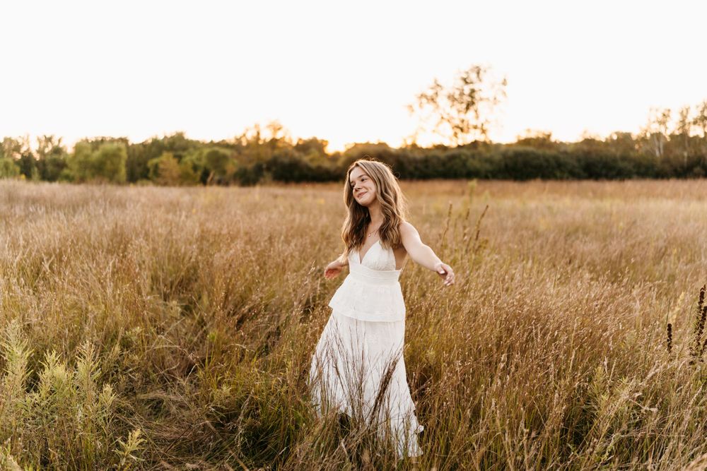 A dreamy portrait in a golden field with a flowing white dress during sunset.