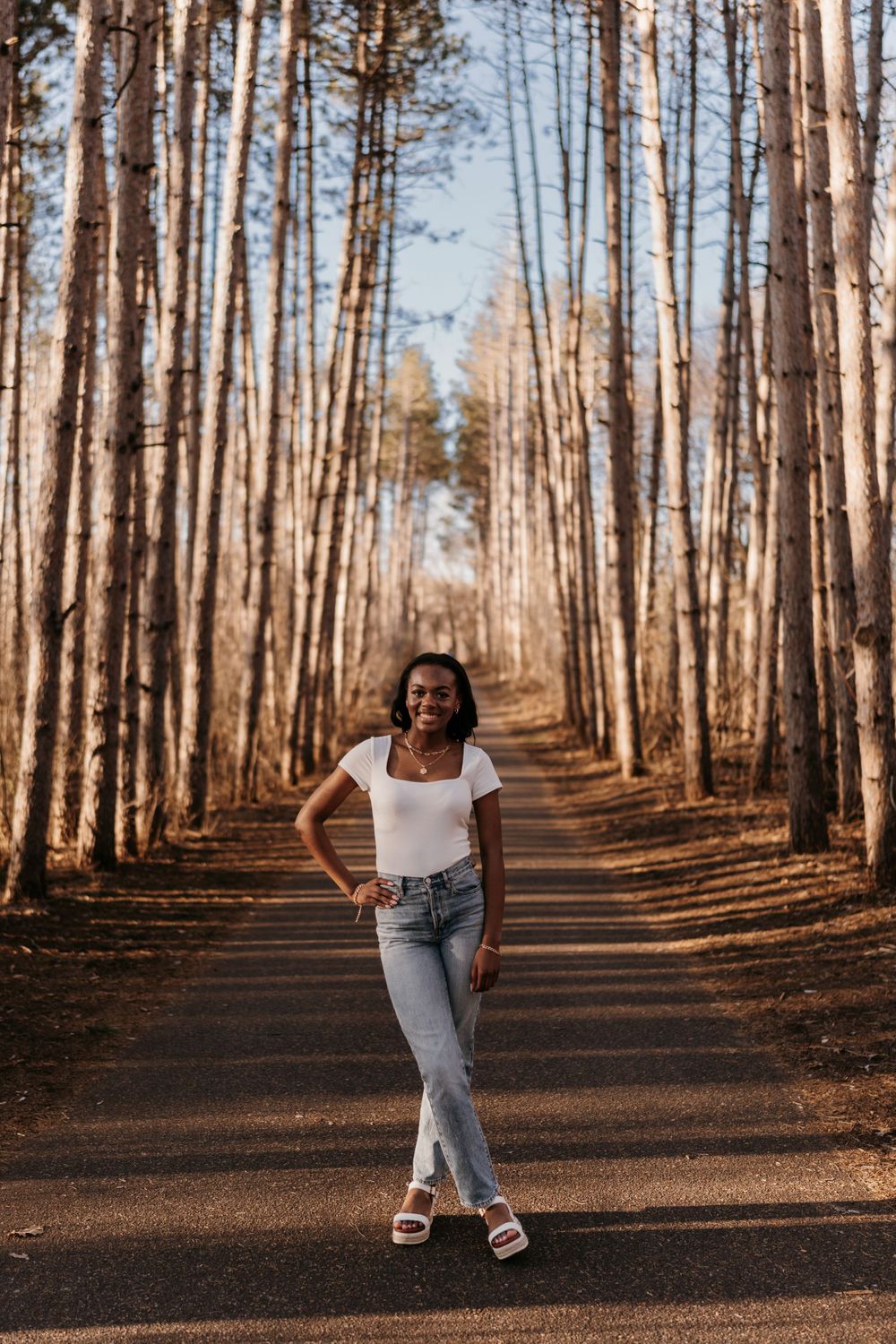 A stylish casual portrait on a tree-lined path in a pine forest.