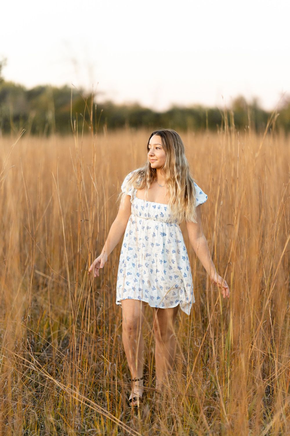 A summery portrait in a floral dress standing among tall wheat grass at golden hour.