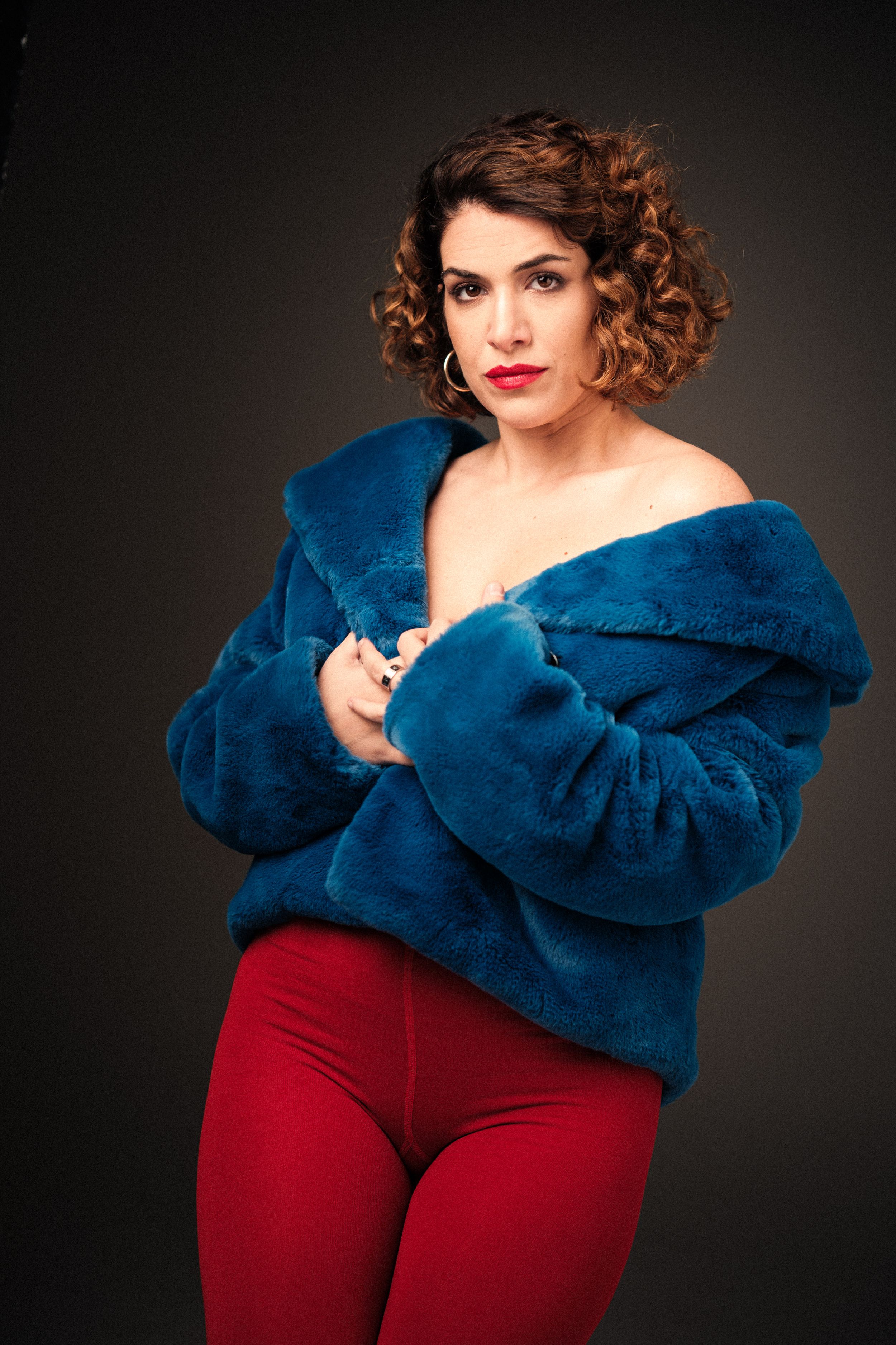 Dramatic pose in royal blue coat and burgundy pants against dark studio background.