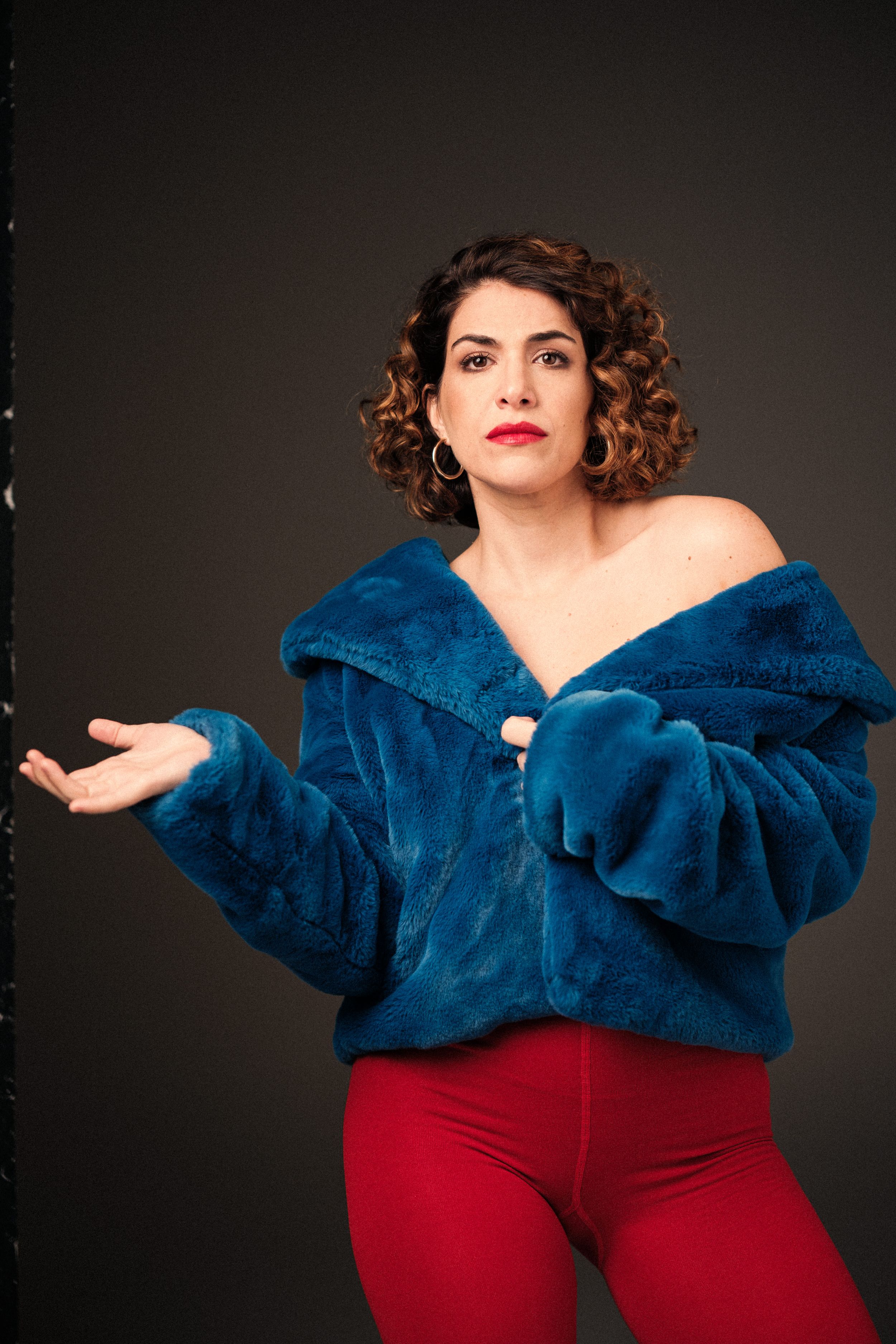 Theatrical poses in luxurious blue fur coat and red pants against dark background.
