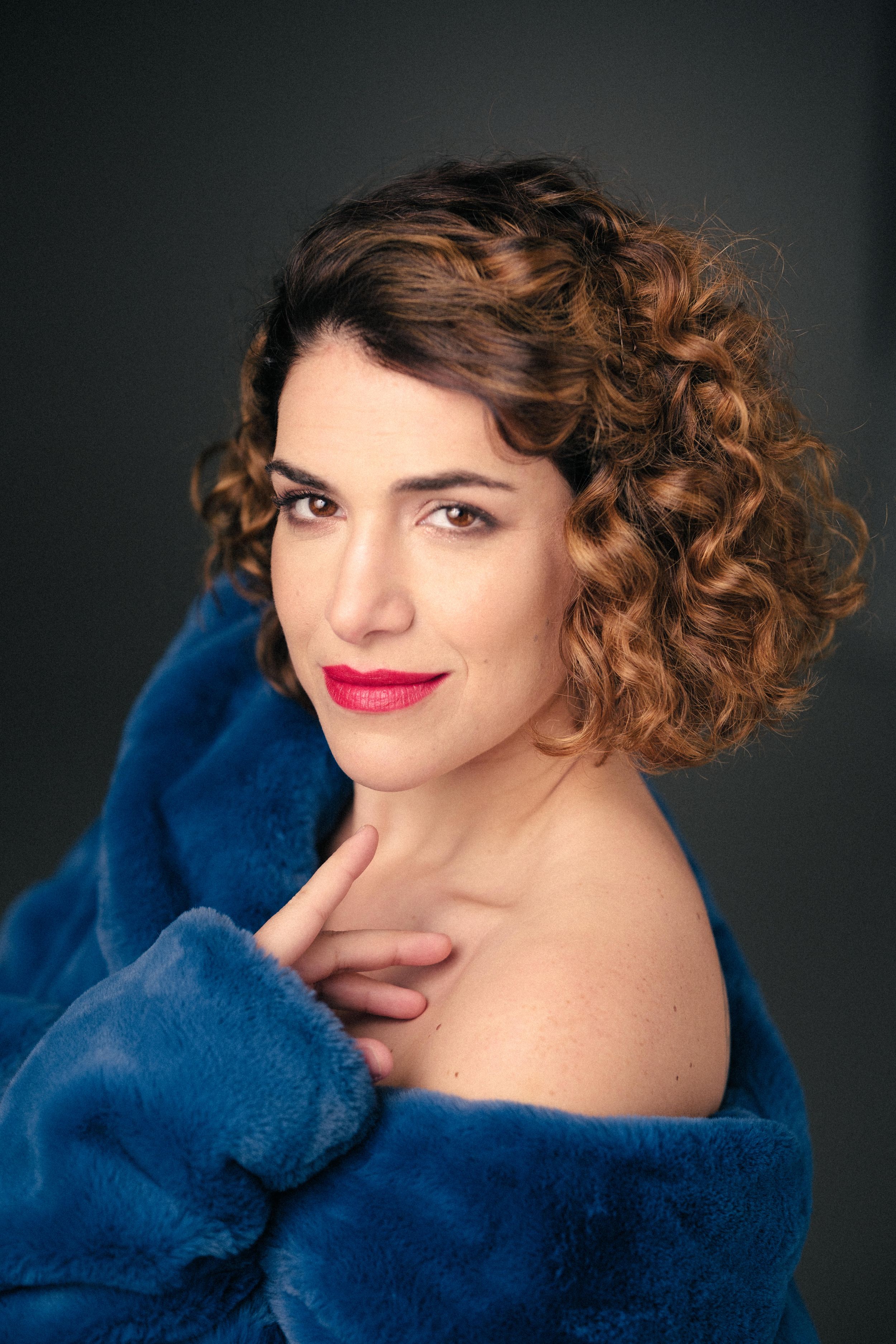 Artistic portrait featuring bright lipstick and blue plush coat in studio setting.